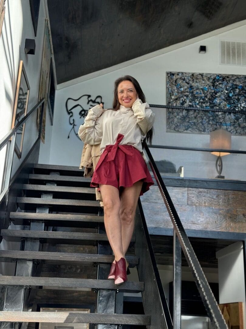 A woman in red skirt and white shirt standing on stairs.