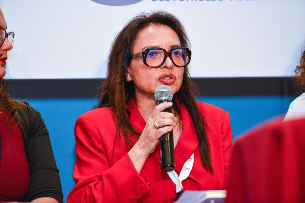 A woman in red jacket holding a microphone.