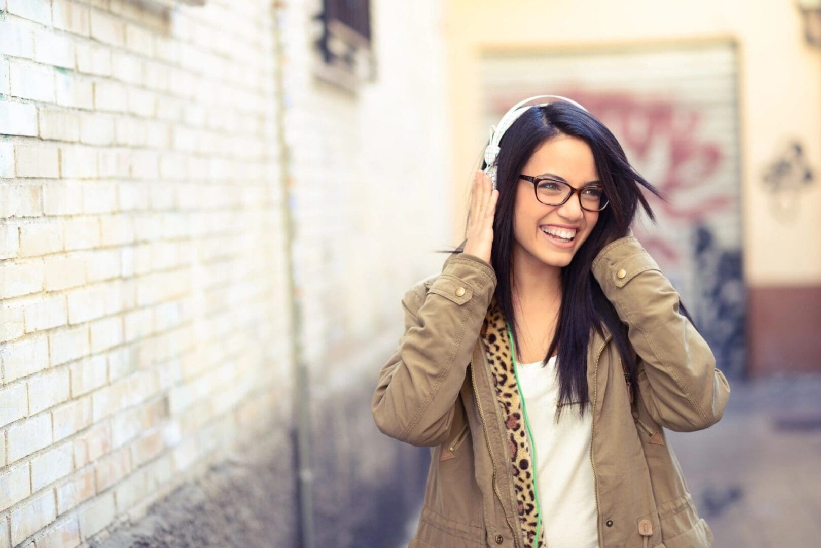 A woman with glasses and headphones is smiling.